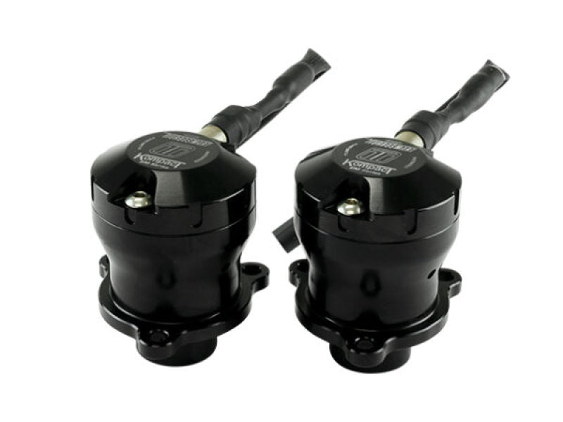 Pair of Turbosmart BOV Kompact EM valves, black anodized, front angled view showing hose fittings and mounting flanges.